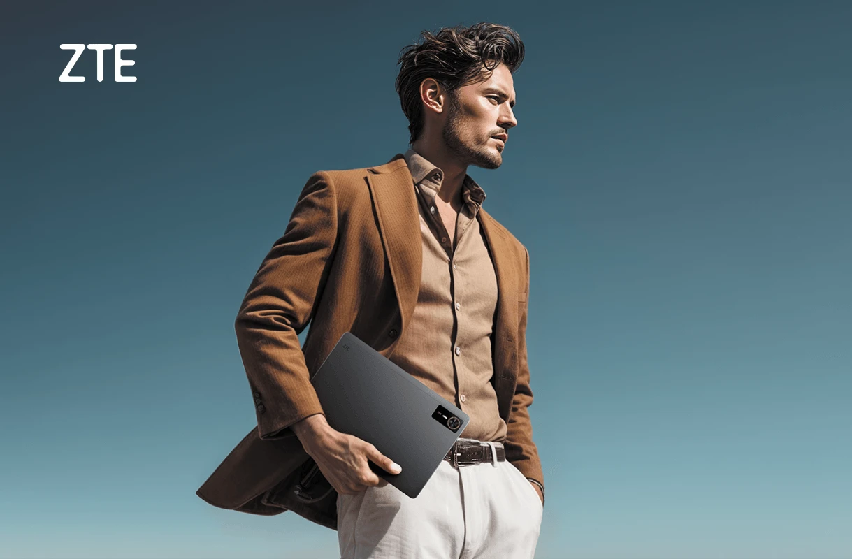 Mężczyzna w brązowym garniturze trzyma tablet ZTE na tle błękitnego nieba.